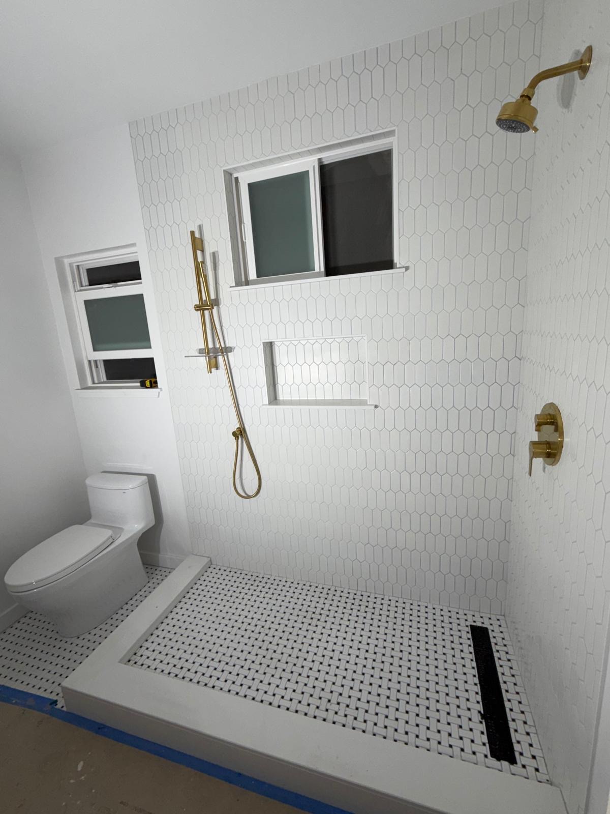 Completed walk-in shower with white hex tile and gold fixtures